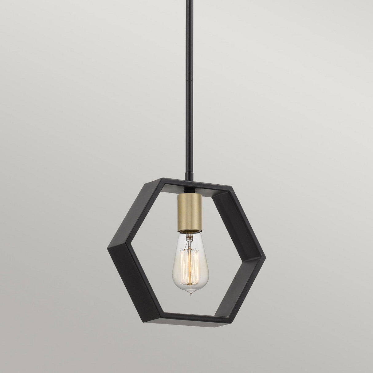The Bismarck 1 Light Mini Pendant - Black showcases a sleek hexagonal black metal frame for a geometric touch, encasing an exposed bulb with a brass socket. It is elegantly suspended by a straight black rod, making it ideal for ambient lighting against any plain background.