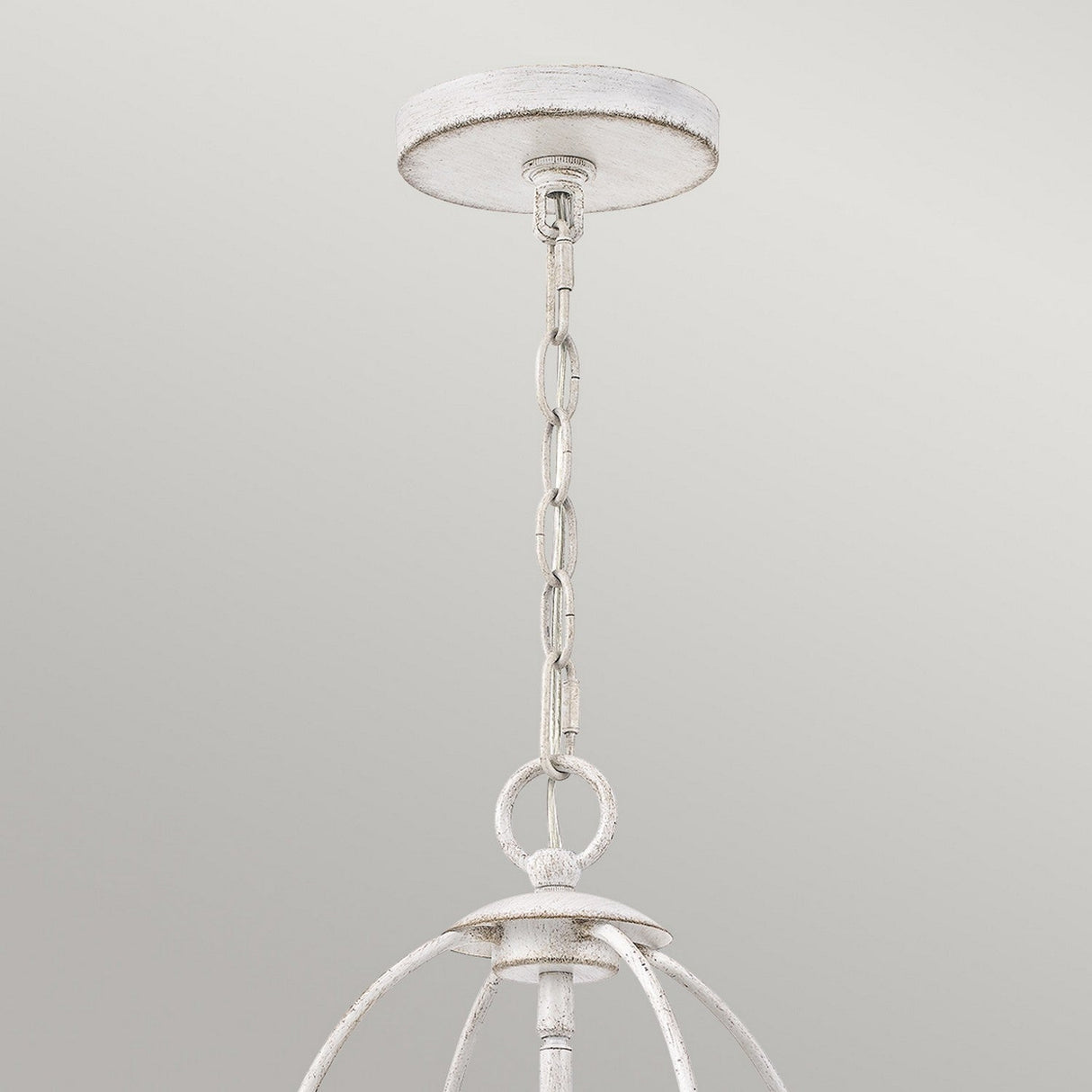 Close-up of the Bradbury 4 Light Chandelier in Antique White, showcasing its rustic hanging light fixture. This four-light design includes a distressed finish, metal loops, and a spherical shape that exudes vintage charm. It is connected to a circular ceiling mount against a plain light grey background.