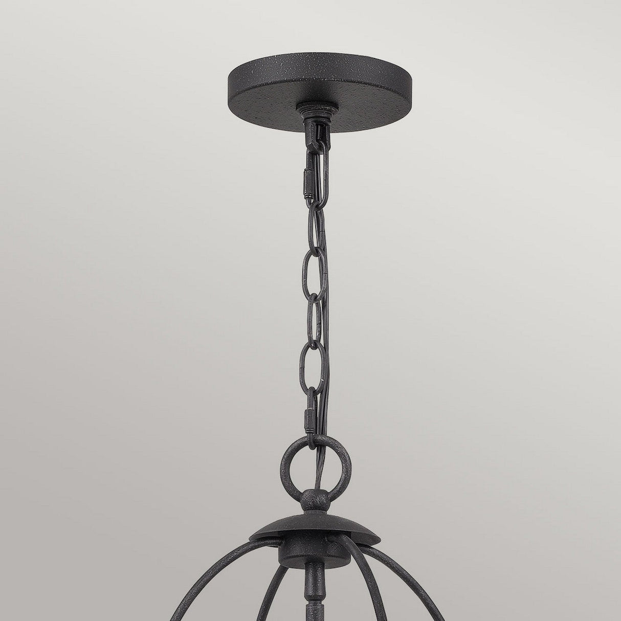 The Bradbury 4 Light Chandelier in Grey Ash showcases a black metal pendant light fixture with a round ceiling mount, linked chain, and curved supports. This versatile design embraces modern aesthetics and hangs elegantly against a light gray background.