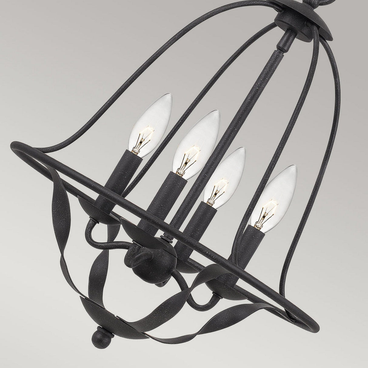 The Bradbury 4 Light Chandelier - Grey Ash features a versatile design with its black metal, cage-like structure and four candle-shaped bulbs arranged in a circular pattern. Decorative curves contribute to its modern aesthetics, making it a standout piece against any plain background.