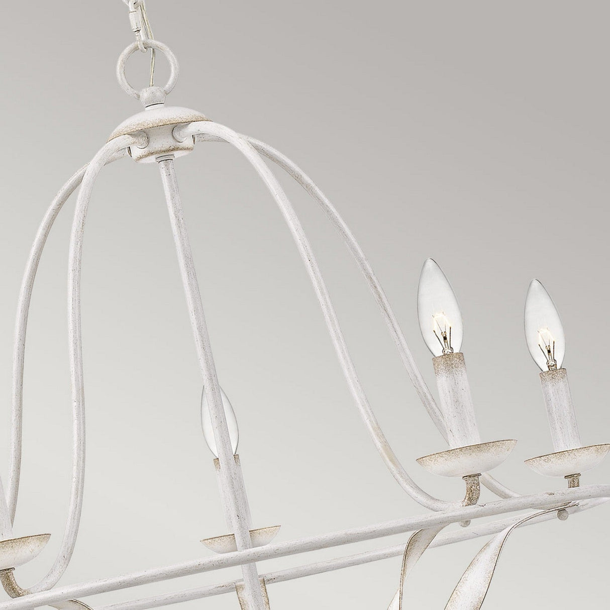 A close-up of the Bradbury 5 Light Chandelier - Antique White showcases its vintage charm, featuring a distressed metal frame and candle-like bulbs, elegantly suspended from a chain against a soft gray background.
