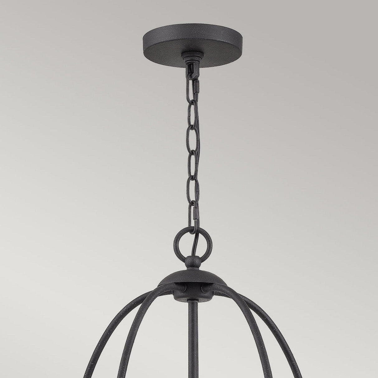 A contemporary flair graces the room as the Bradbury 5 Light Chandelier - Grey Ash hangs from the ceiling, suspended by a chain. Its curved metal bars form an open, spherical shape, offering a modern chandelier design. The matte-finished ceiling mount contrasts elegantly with the Grey Ash background.