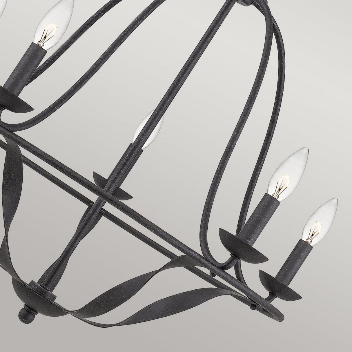 Close-up of the Bradbury 5 Light Chandelier in Grey Ash, showcasing its black metal industrial design and modern style with five candle-shaped bulbs supported by elegant curving metal arms against a light gray background.