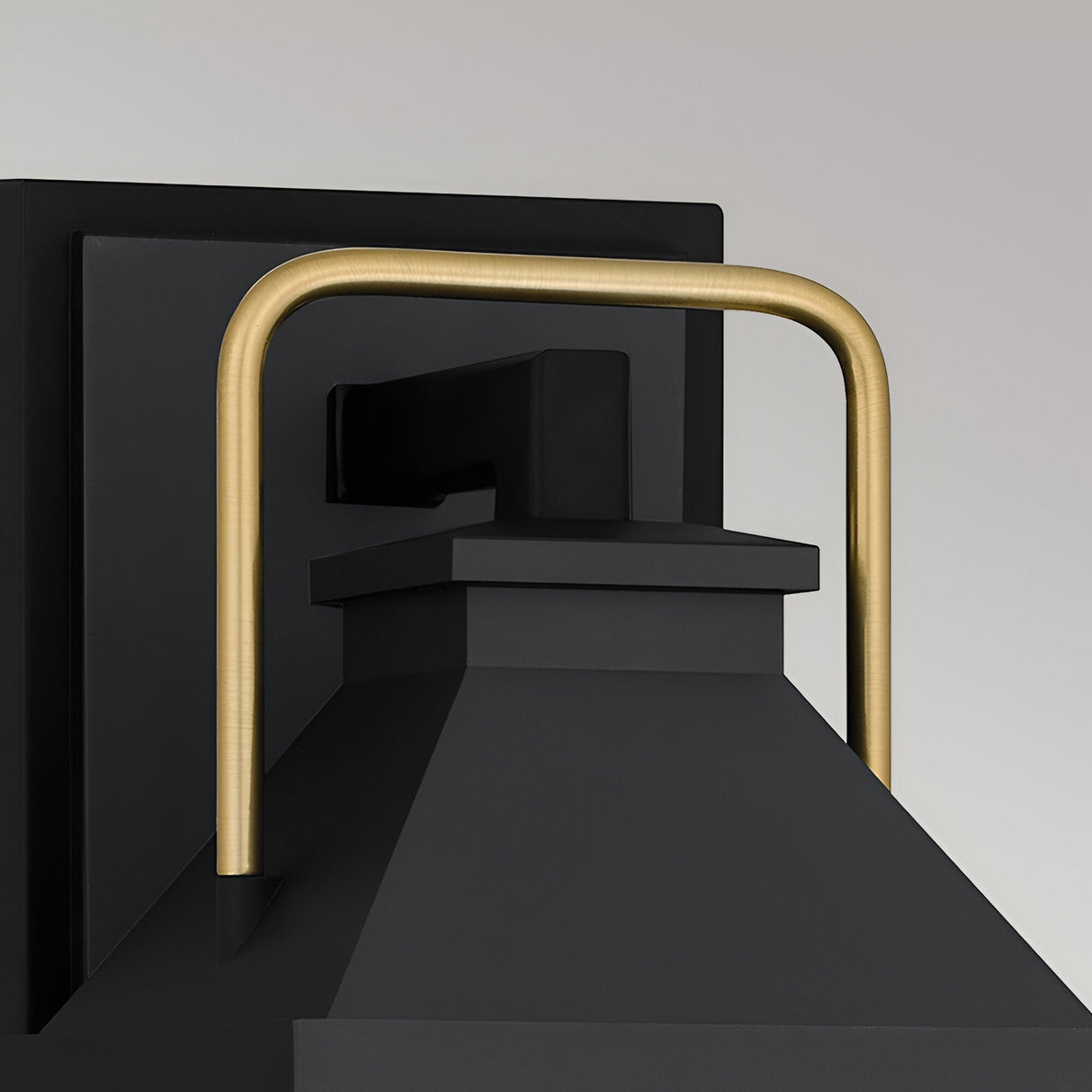 A close-up of the Buckley 1 Light Coastal Small Outdoor Wall Lights Lantern in black, featuring a matte black base and a rectangular gold handle arching over the top, set against a plain light gray background.