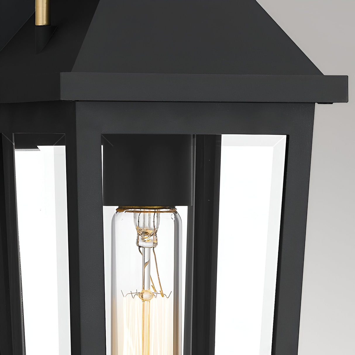 Close-up of the Buckley 1 Light Coastal Small Outdoor Wall Lights Lantern in black, featuring clear glass panels and a vertical tubular bulb, set against a softly lit plain background.