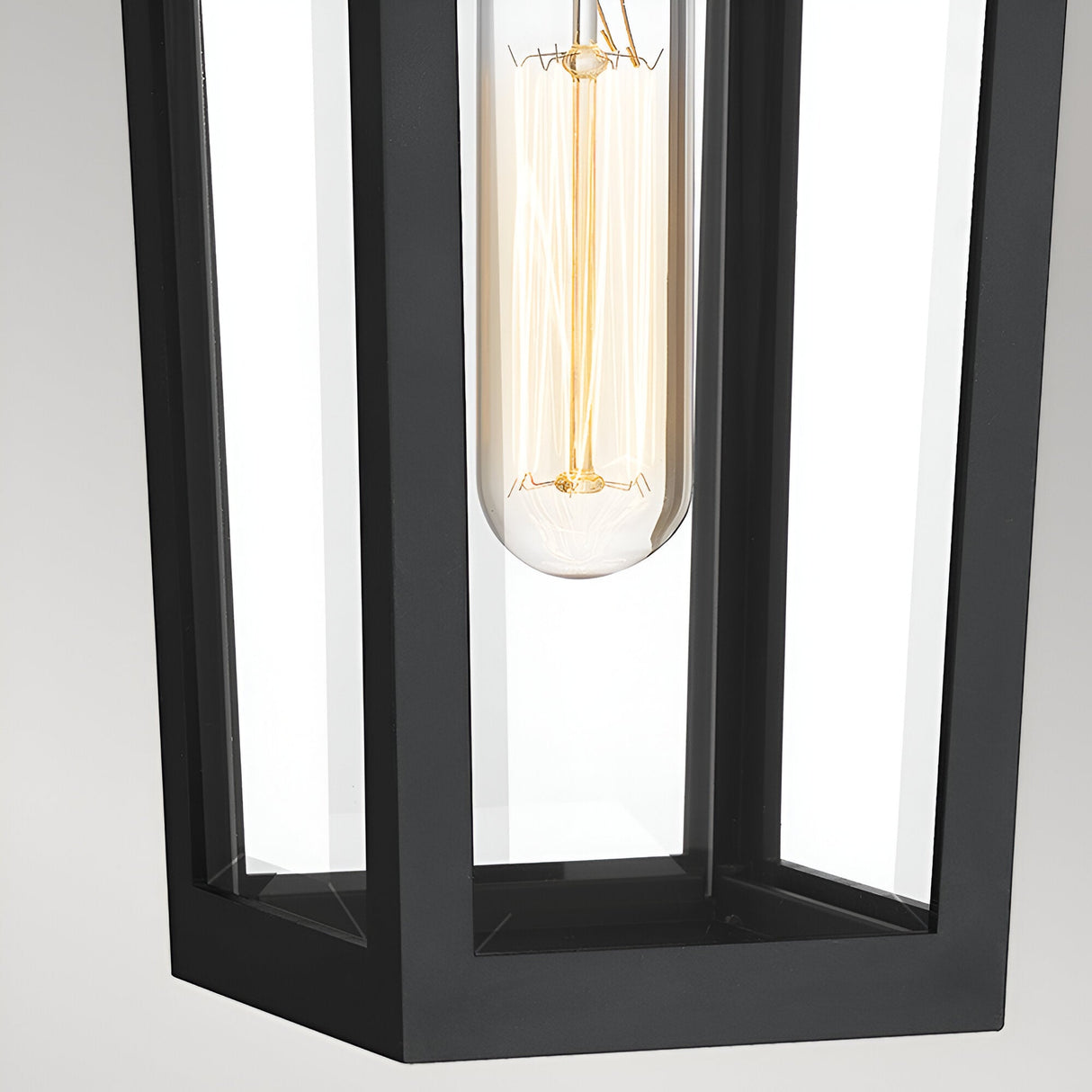 Close-up of the Buckley 1 Light Coastal Small Outdoor Wall Lights Lantern in black, showcasing a modern rectangular metal and glass design with a clear vintage Edison bulb emitting a warm glow.