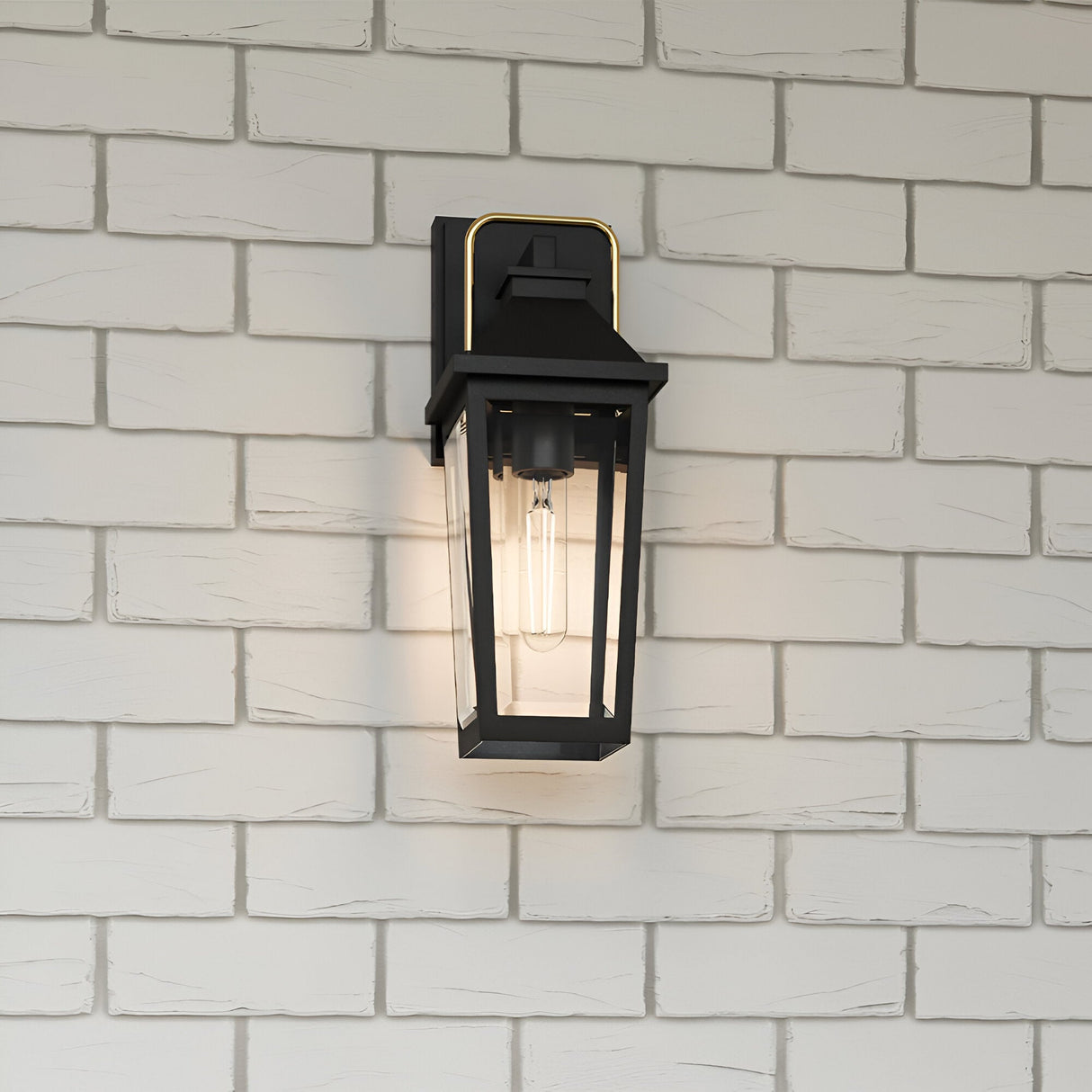 The Buckley 1 Light Coastal Small Outdoor Wall Lights Lantern in black, with a clear glass enclosure and exposed bulb, is mounted on a white brick wall and emits a soft, warm glow—perfect for stylish coastal outdoor lighting.