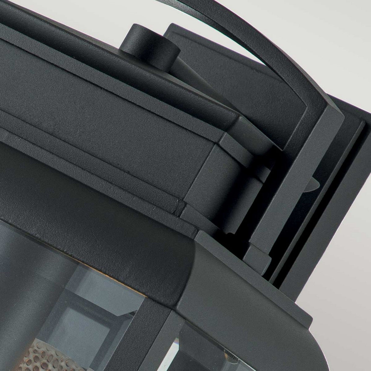 Close-up of the Byron Outdoor 1 Light Large Wall Lantern in a sleek graphite finish. The modern geometric design showcases a square frame and bevelled glass panels, offering a view of the bulb inside. Its contemporary appearance is enhanced against a plain background by its grey reflector detail.