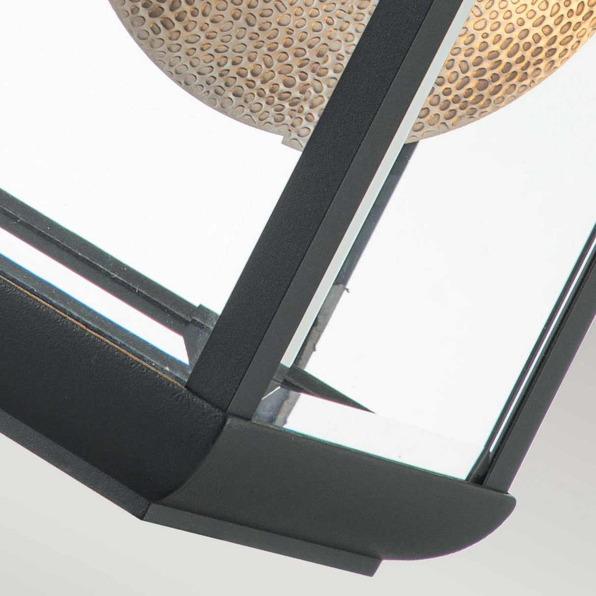 Close-up of the Byron Outdoor 1 Light Large Wall Lantern in a graphite finish, featuring a metal and glass enclosure with an inside textured perforated design. The dark frame showcases sleek lines and beveled glass, embodying a blend of contemporary style and subtle detailing.