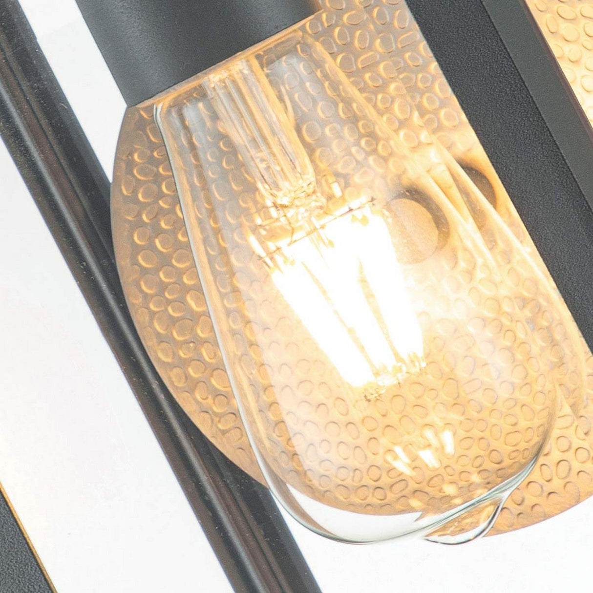 Close-up of a glowing incandescent light bulb encased within a textured, honeycomb-patterned glass cover. This light is featured in the Byron Outdoor 1 Light Small Wall Lantern, which has an IP44-rated black metal fixture with a graphite finish and grey reflector, creating a warm and inviting ambiance ideal for outdoor spaces.