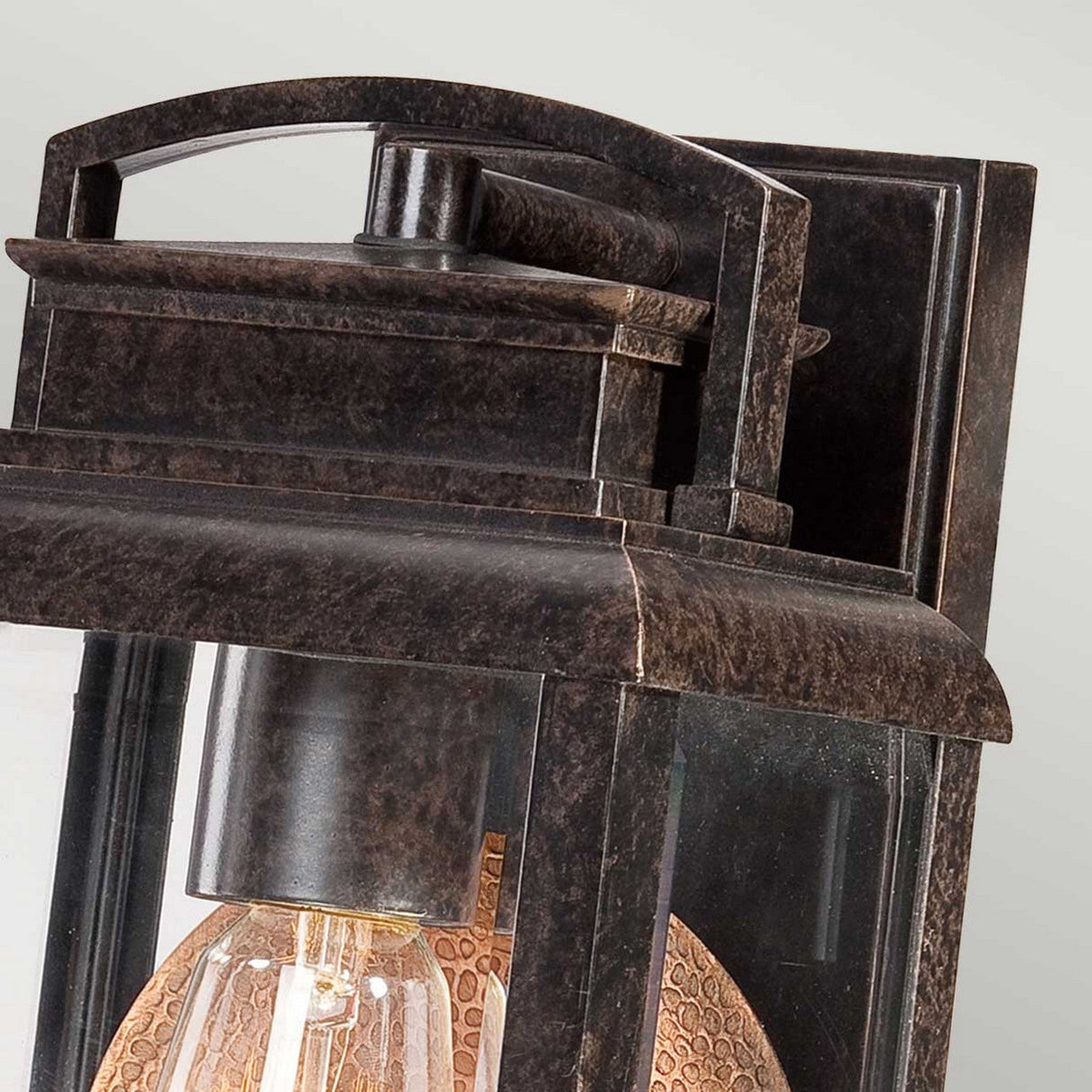 Close-up of the Byron Outdoor 1 Light Small Wall Lantern, featuring a textured bulb encased in clear glass. Its frame, finished in Imperial Bronze, enhances its antique appeal, and the copper reflector contributes warmth to its vintage charm.