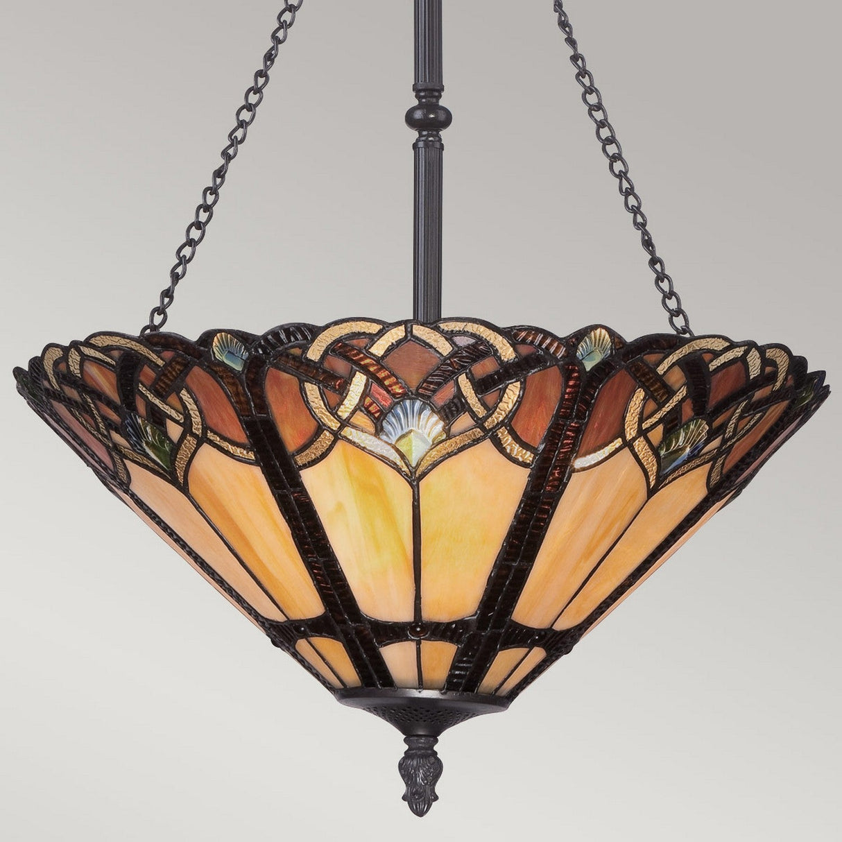 The Cambridge 3 Light Pendant Chandelier in Vintage Bronze showcases an Art Deco-style design with Tiffany-style stained glass panels in warm amber, brown, and green hues. It features intricate geometric patterns that add charm as it hangs elegantly from a dark metal chain.