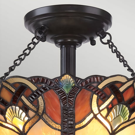 A close-up view of the Cambridge 2 Light Large Tiffany Semi-Flush showcases intricate geometric patterns in shades of red, orange, yellow, and green. Suspended by dark metal chains and featuring a vintage bronze finish, this elegant design adds a touch of sophistication.