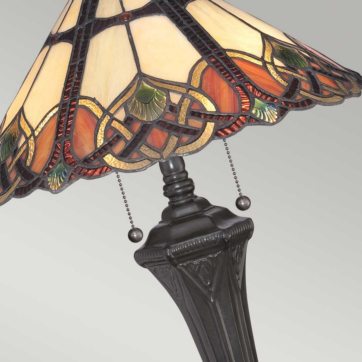 Close-up of the Cambridge 2 Light Table Lamp - Vintage Bronze, featuring a stained glass shade with intricate patterns in orange, green, and cream. The lamp includes a vintage bronze base with ornate detailing and two pull chains.