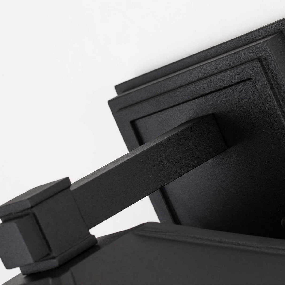 A close-up of the Cedar Point Outdoor 1 Light Large Wall Lantern in black reveals its sleek design with a rectangular base and angled arm, reminiscent of a modern, minimalistic lantern. Featuring clean lines and a matte finish, this IP44-rated fixture is securely mounted on a white wall.