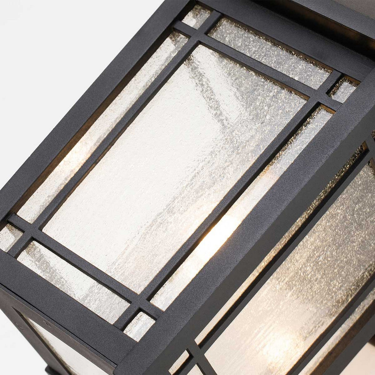 Close-up of the Cedar Point Outdoor 1 Light Large Wall Lantern in black, featuring an IP44 rating. The wall lantern has textured glass panels with a glowing light visible inside. Its geometric and modern design highlights straight lines and a minimalist aesthetic.