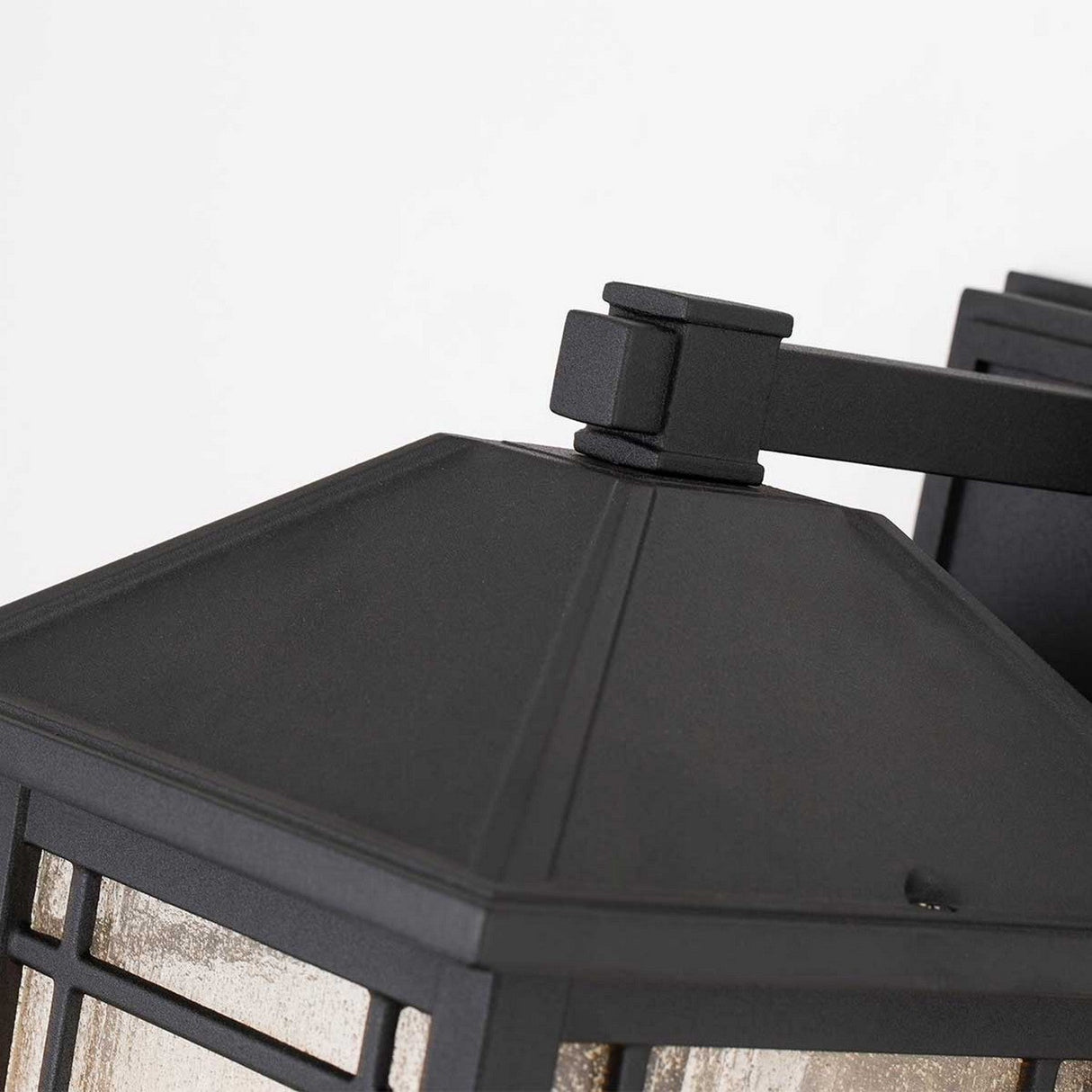 Close-up of the Cedar Point Outdoor 1 Light Medium Wall Lantern - Black, showcasing its pyramid-shaped top and seedy glass panels. This outdoor lighting fixture is mounted on a wall bracket, effortlessly merging modern and classic design elements.