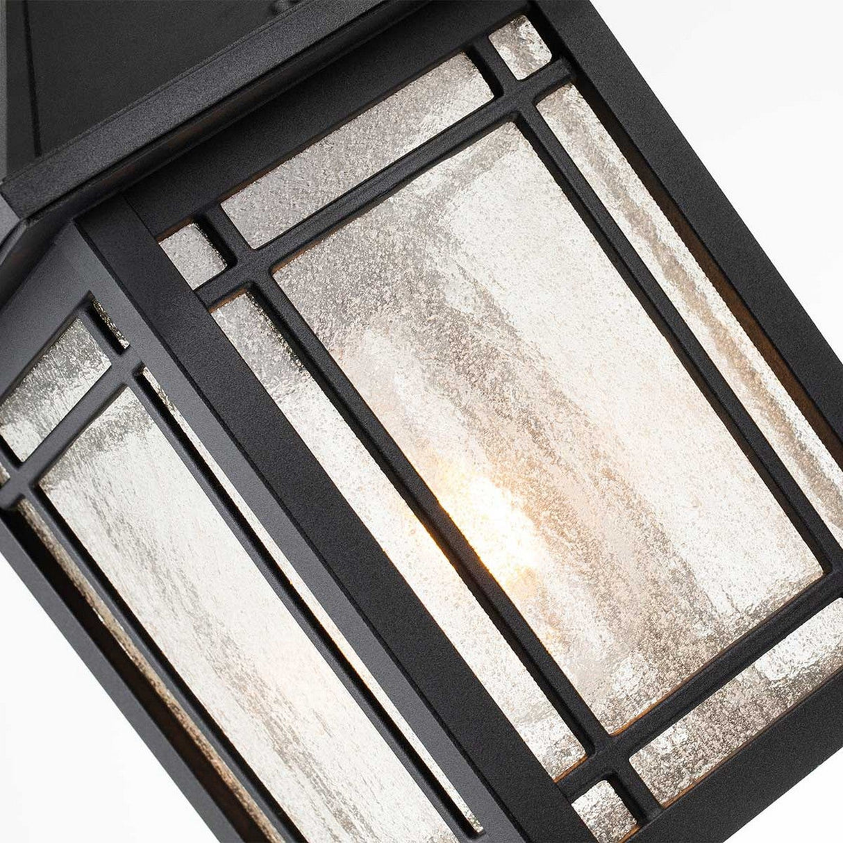 A close-up of the Cedar Point Outdoor 1 Light Chain Pendant in black highlights its rustic elegance with frosted glass panels. Inside, a warm light accentuates the textured surface. Its geometric design is both modern and elegant, making it an ideal choice for outdoor spaces.