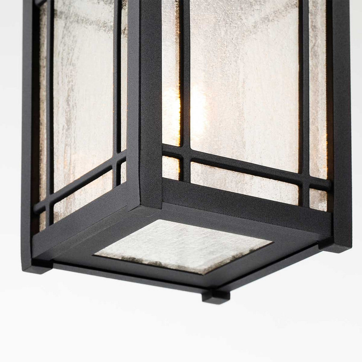 Close-up of the Cedar Point Outdoor 1 Light Chain Pendant in black, showcasing a rectangular lantern design that exudes rustic elegance. The seedy glass panels feature a textured finish, casting a warm glow, while its sides boast a grid-like pattern reminiscent of outdoor chain pendants.