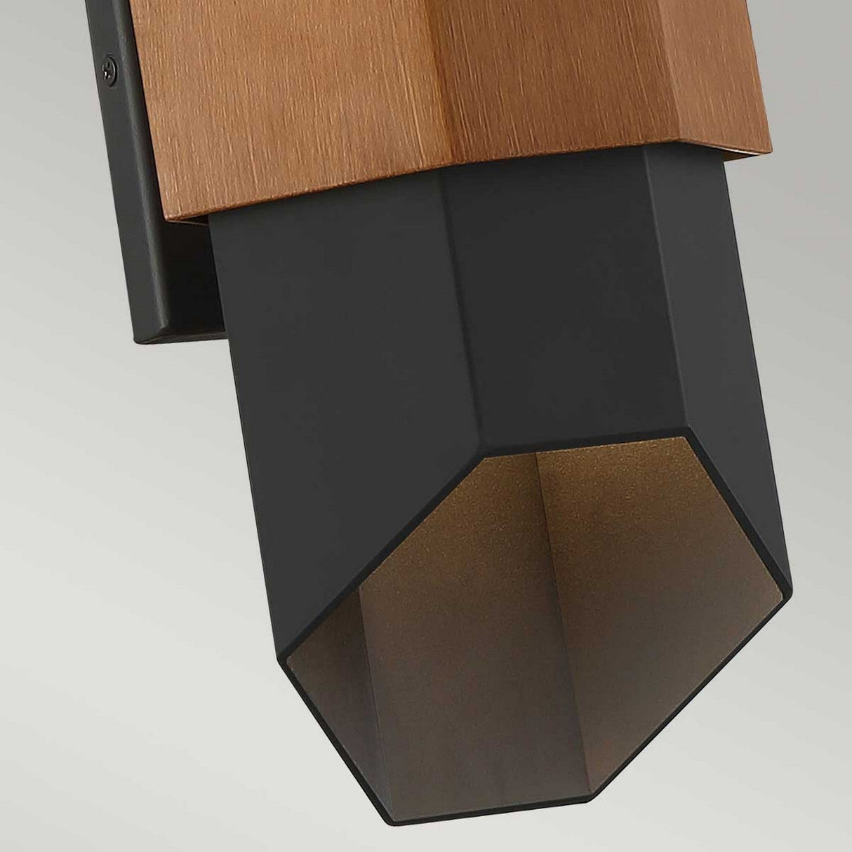 Close-up of the Chasm Outdoor LED Medium Wall Lantern in matte black, showcasing its geometric design with an energy-efficient lighting element. The lantern features a black hexagonal pattern that extends downward, creating a contrast against the copper-colored mounting plate. This piece, resembling a lantern, is shown unlit in the image.