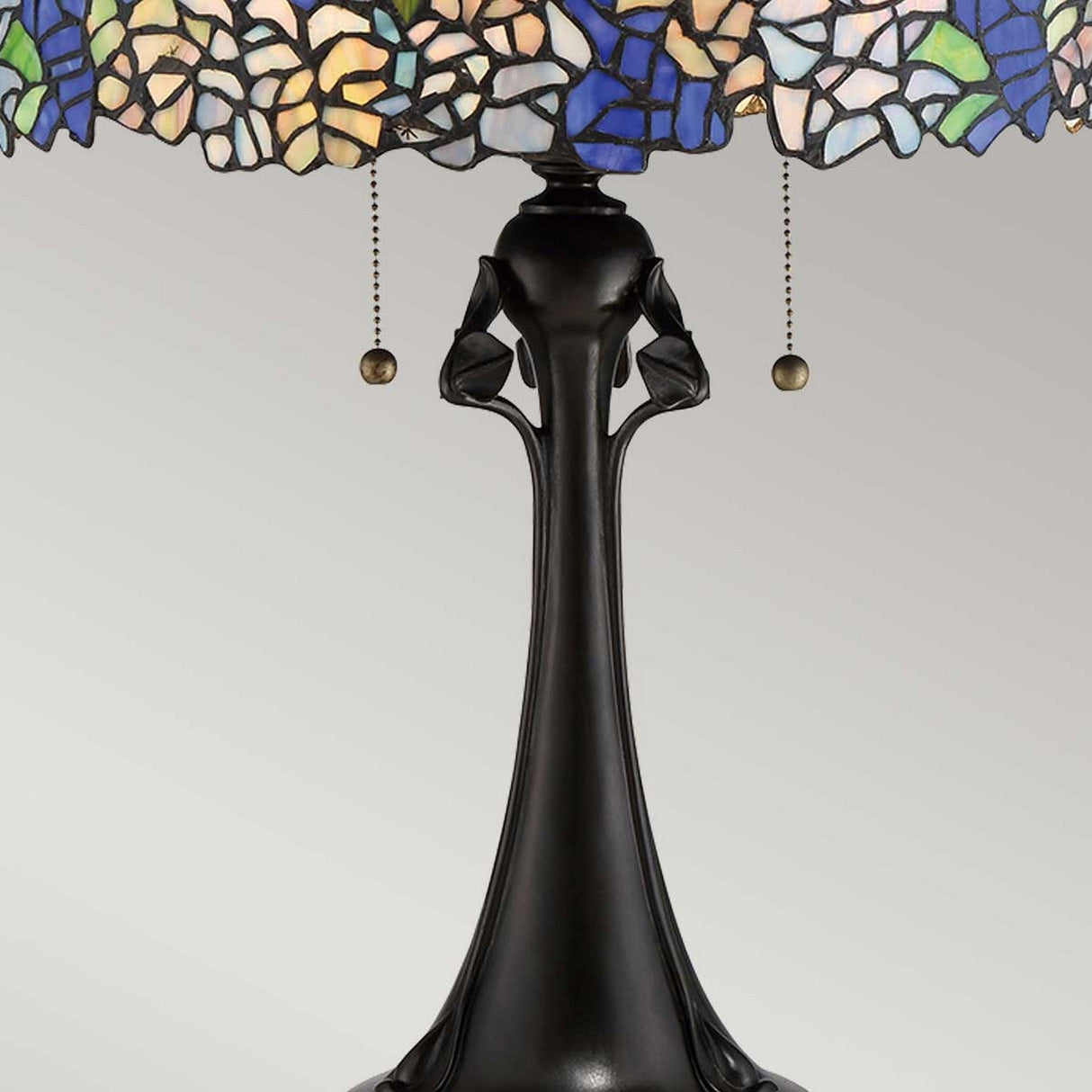 The Cobalt 3 Light Tiffany Table Lamp - Vintage Bronze illustrates a hydrangea pattern in its decorative stained glass shade, featuring blue, green, and beige hues. The lamp is complemented by a dark, ornate Vintage Bronze base with two pull chains elegantly suspended beneath the shade.