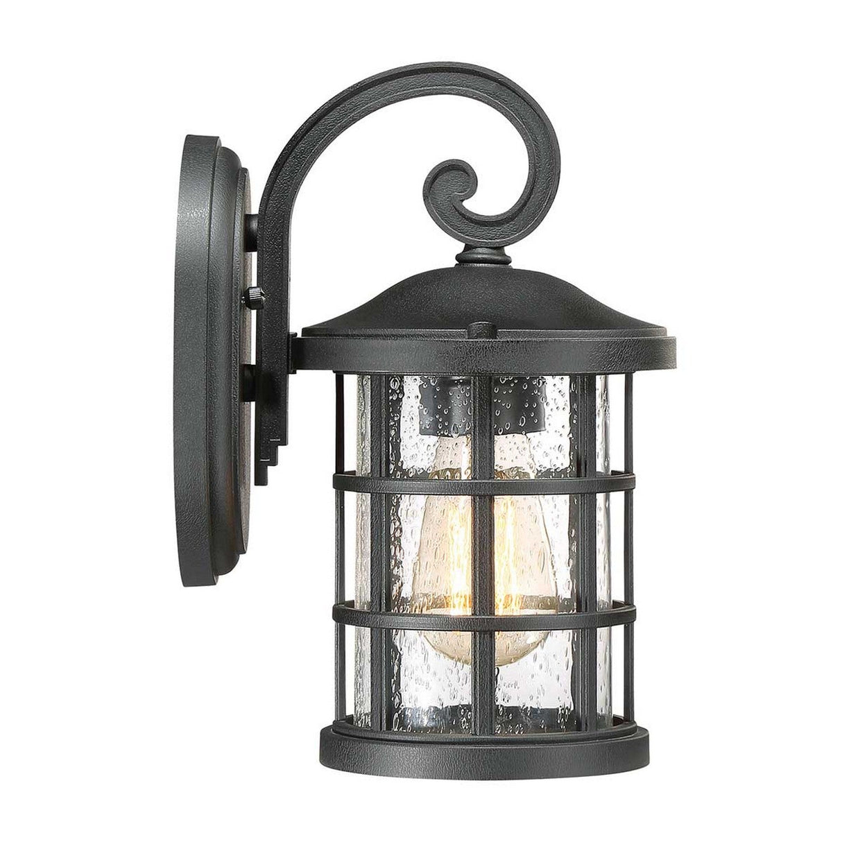 The Crusade Outdoor 1 Light Small Wall Lantern - Black showcases a Craftsman design, featuring a cylindrical seeded glass shade with a grid pattern. A warm light bulb glows inside, and the fixture is mounted on a curved arm attached to a wall plate, adding rustic charm to any exterior space.