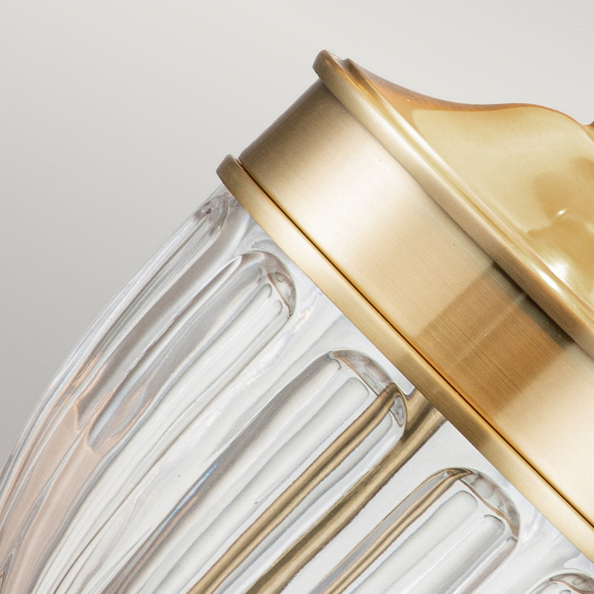 Close-up of the Dennison 1 Light Table Lamp with a textured, ribbed glass design and a brushed brass finish. The lamp is angled to showcase the striking contrast between the clear glass and polished metal—a perfect touch for elegant home decor.