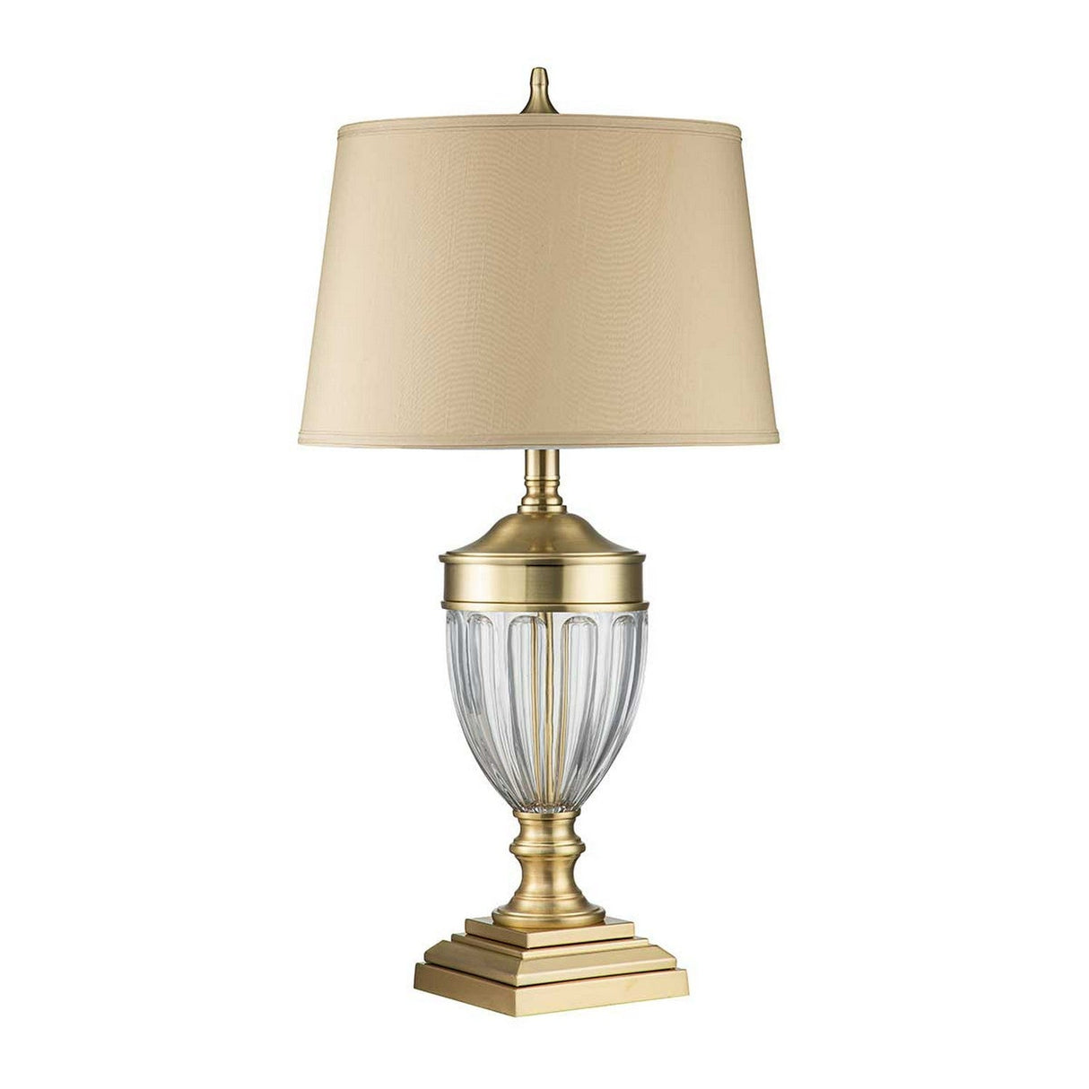 The Dennison 1 Light Table Lamp in brushed brass showcases a clear glass base with vertical grooves and an elegant square pedestal. It features a slightly tapered beige lampshade, creating an exquisite design that adds traditional elegance to any home decor.