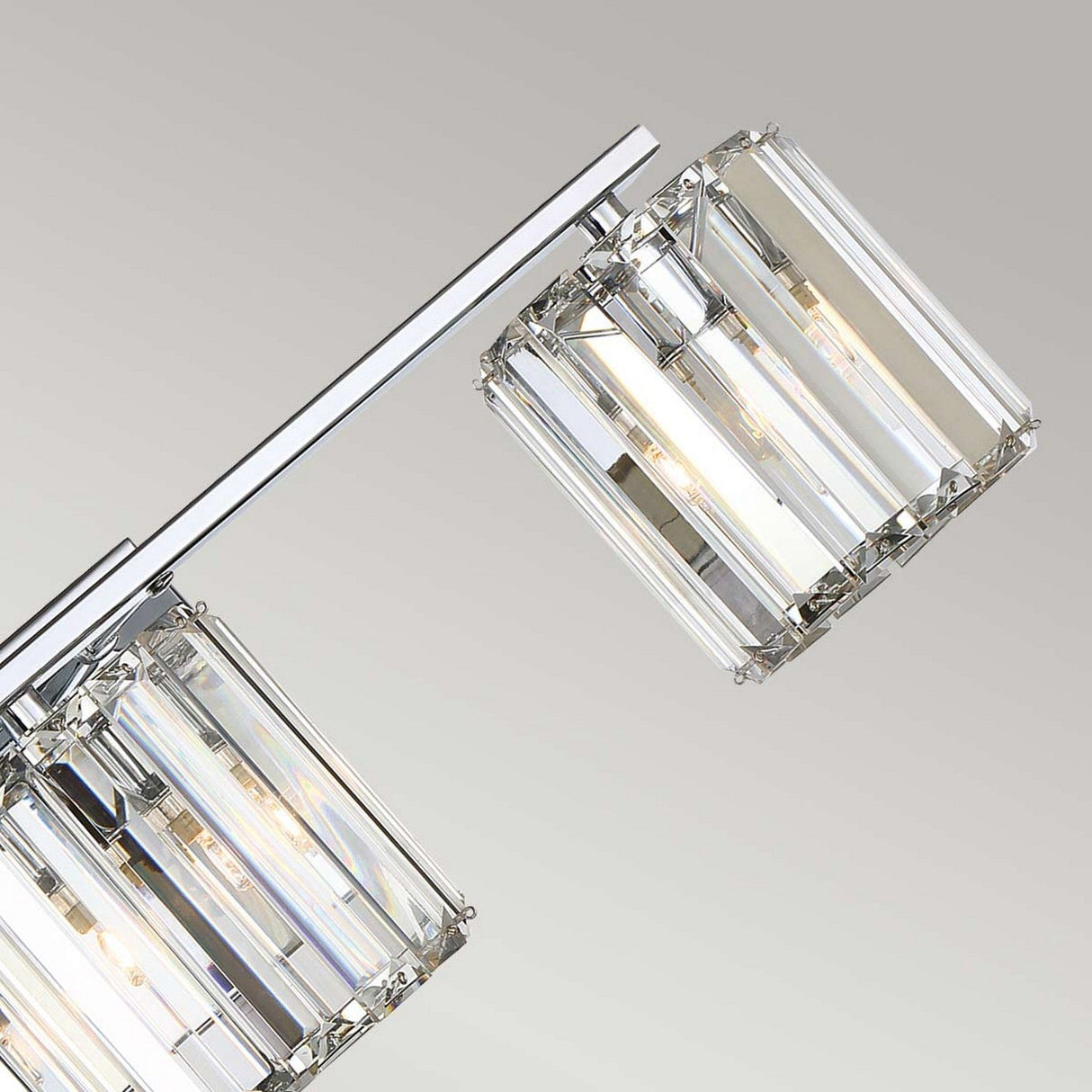 Close-up of the Divine 3 Light Wall Light - Polished Chrome, featuring a modern fixture with two rectangular crystal glass shades along a sleek, polished chrome pole. The minimalist design exudes elegance as the crystals beautifully capture light against a light grey background.
