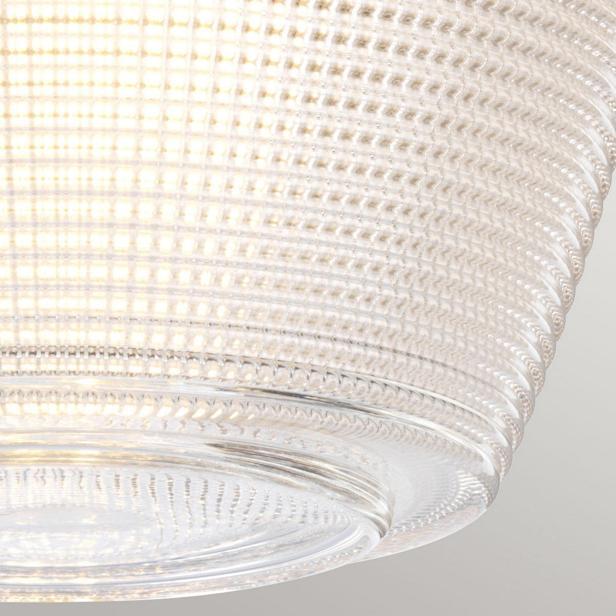 A close-up of the Dublin 1 Light Semi Flush in polished chrome reveals its textured, transparent glass design in a contemporary style, casting a warm, soft glow. The glass's intricate pattern produces a layered effect that enhances light diffusion. It's set against a simple, neutral-colored wall, perfect for sleek bathroom lighting.