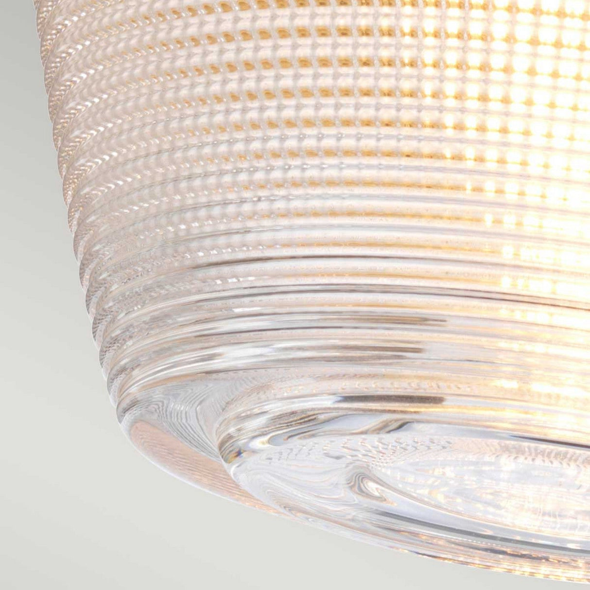 A close-up view of a textured glass light fixture features a ribbed pattern similar to the Dublin 1 Light Semi Flush - Natural Brass. This illuminated piece highlights its detailed design and casts a warm glow, ideal for enhancing bathroom lighting against the plain, neutral background.