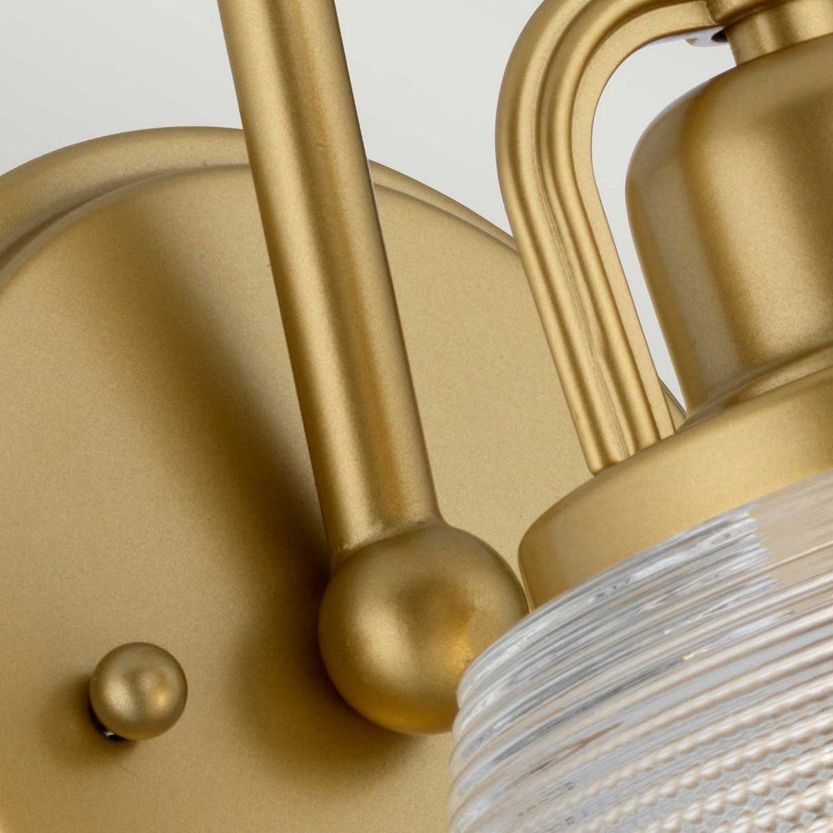 A close-up of the Dublin 1 Light Wall Light in Natural Brass, featuring a round base and a glass shade with concentric ridges. Perfect for bathroom lighting, it adds an elegant touch to any space.