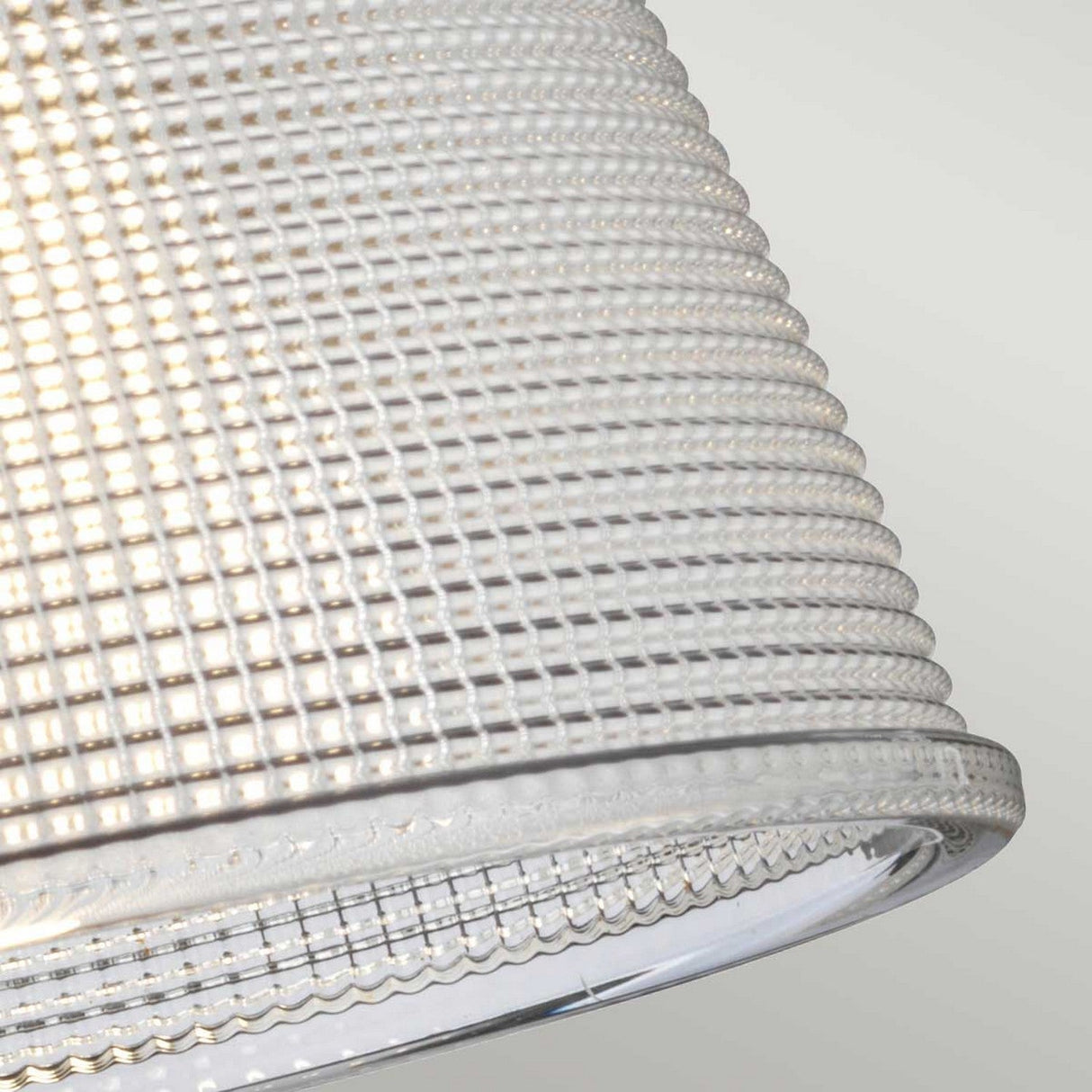 A close-up of the textured glass shade features a grid pattern showcasing its intricate details. The clear glass allows for a soft glow, making it perfect for enhancing bathroom lighting. Set against a neutral backdrop, it pairs beautifully with the Dublin 1 Light Wall Light in Natural Brass.