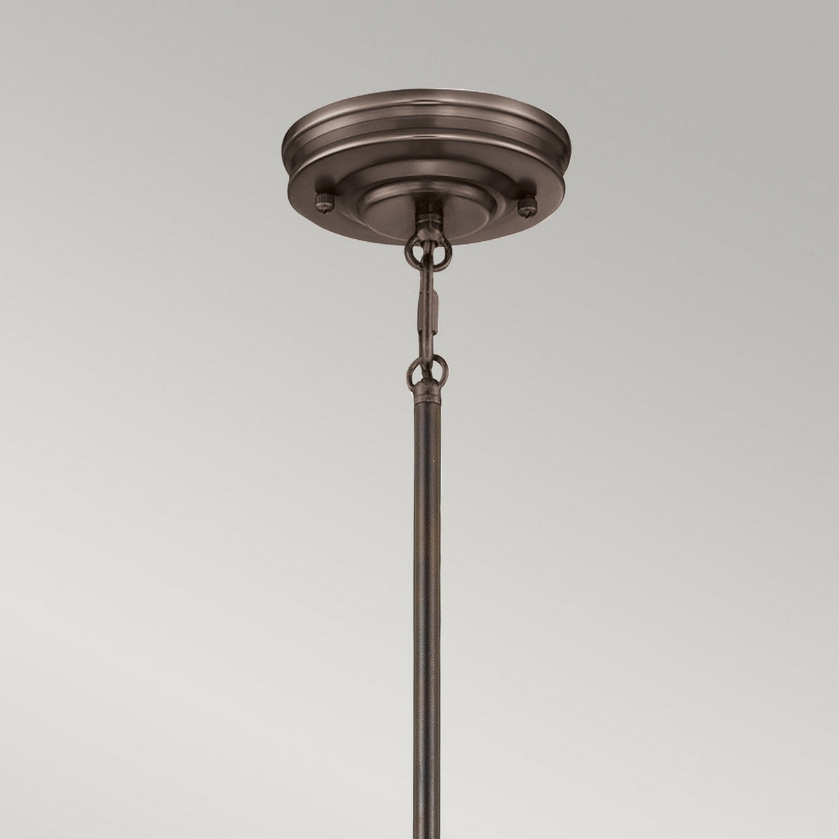 An up-close look at the Emery 1 Light Medium Pendant in a Palladian Bronze finish, featuring a vintage-inspired design with a rod and chain attachment. The background is a plain, light gray color.