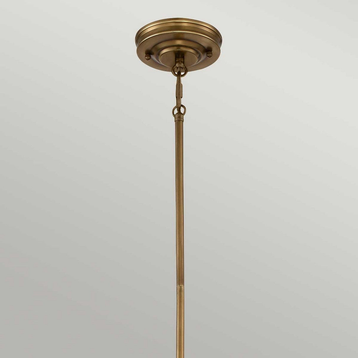 A rustic farmhouse lighting fixture, the Emery 1 Light Mini Pendant - Weathered Brass elegantly attaches to the ceiling with its bronze ceiling rod and decorative round base. Its chain link connection and weathered brass finish lend it a timeless charm, standing vertically against a light gray background.