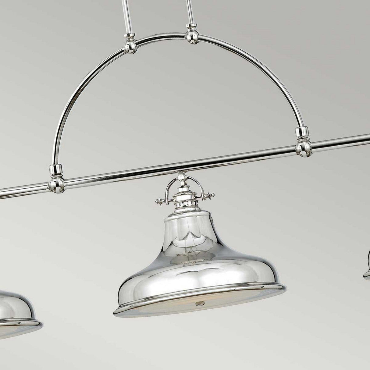 The Emery 3 Light Island Pendant - Imperial Silver is an elegant and contemporary lighting fixture, featuring a reflective finish and suspended from a gracefully curved rod. Its minimalist design highlights smooth, rounded edges with an industrial flair, making it an ideal match for the vintage Americana aesthetic when placed against a light-colored background.