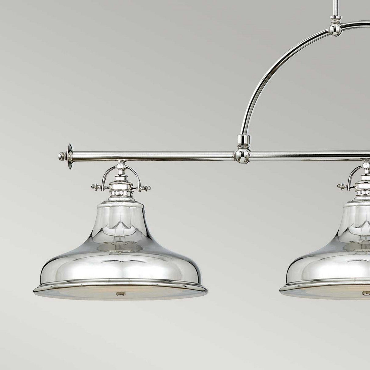 A close-up view showcases two shiny fixtures from the Emery 3 Light Island Pendant in Imperial Silver, both attached to a metallic horizontal bar with a curved rod. The sleek, reflective design radiates vintage Americana charm against a neutral, light gray background.