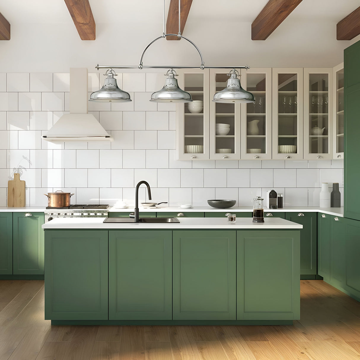 A contemporary kitchen features green cabinetry and a white countertop island. Suspended above are the Emery 3 Light Island Pendants in Imperial Silver, which infuse the space with vintage Americana charm. The backdrop includes a white range hood against a tiled backsplash, with glass-fronted upper cabinets showcasing dishes and wooden beams accentuating the ceiling.