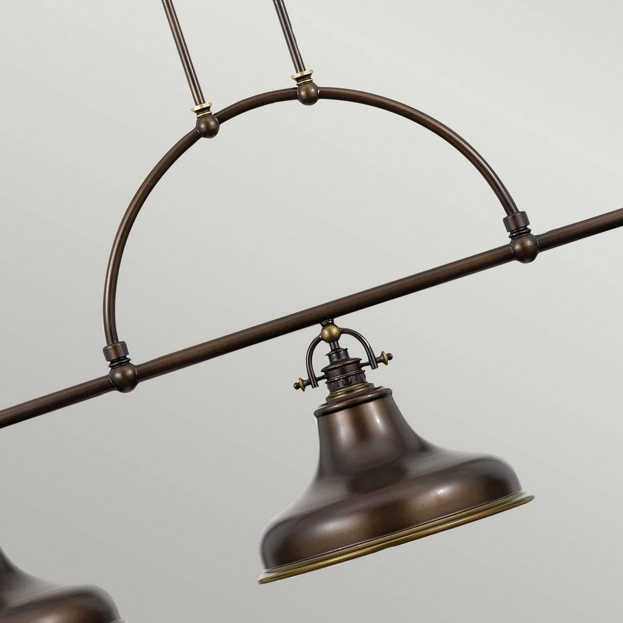 Close-up of the Emery 3 Light Island Pendant in Palladian Bronze, featuring a vintage-style fixture with a domed shade and metal arch design. Suspended from two rods, it exudes rustic charm with its industrial aesthetic against a plain, light background.