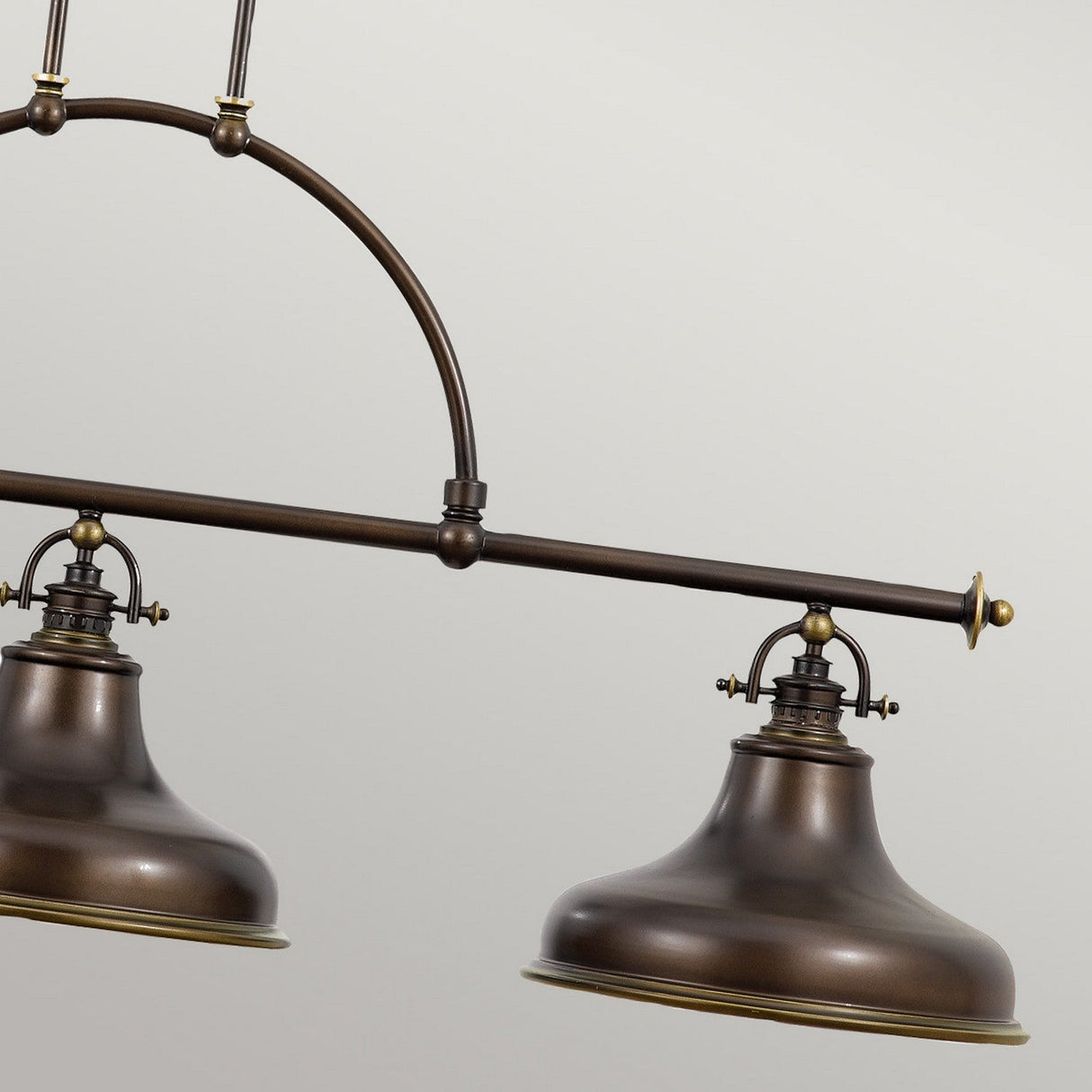 A close-up of the Emery 3 Light Island Pendant showcases its vintage style, featuring two metal dome-shaped lampshades with a Palladian Bronze finish that exudes rustic charm. They are gracefully suspended from a curved rod against a neutral background.