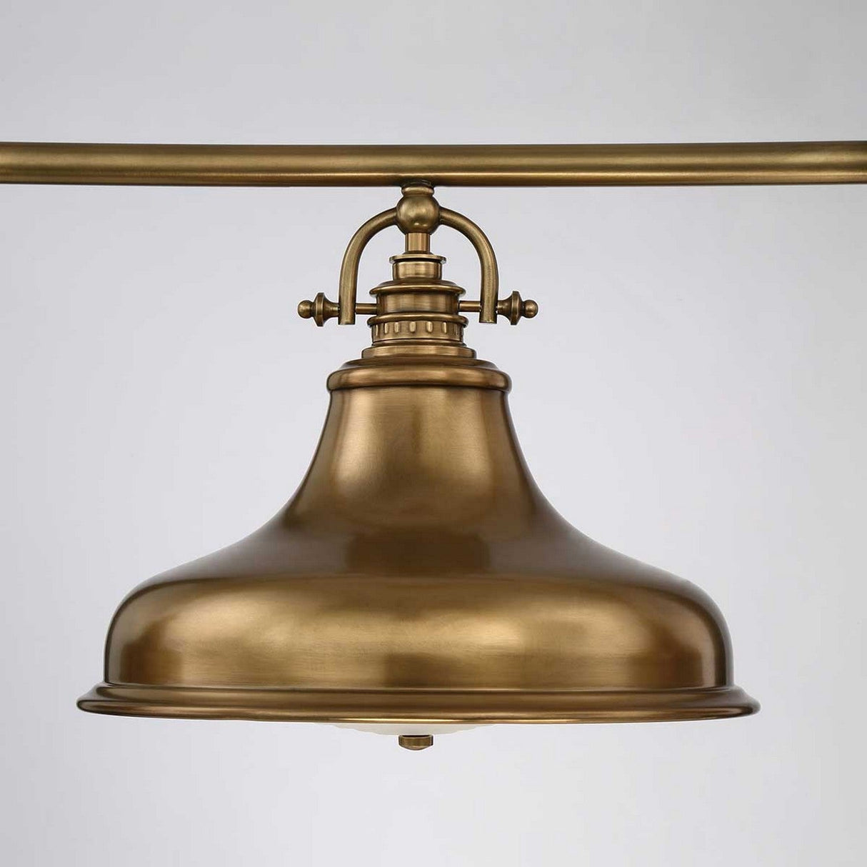 The Emery 3 Light Island Pendant in Weathered Brass showcases a vintage-inspired design with a wide, bell-shaped shade crafted from weathered brass and suspended from a horizontal rod. The metal's smooth, shiny finish enhances its industrial aesthetic against a plain light gray background.