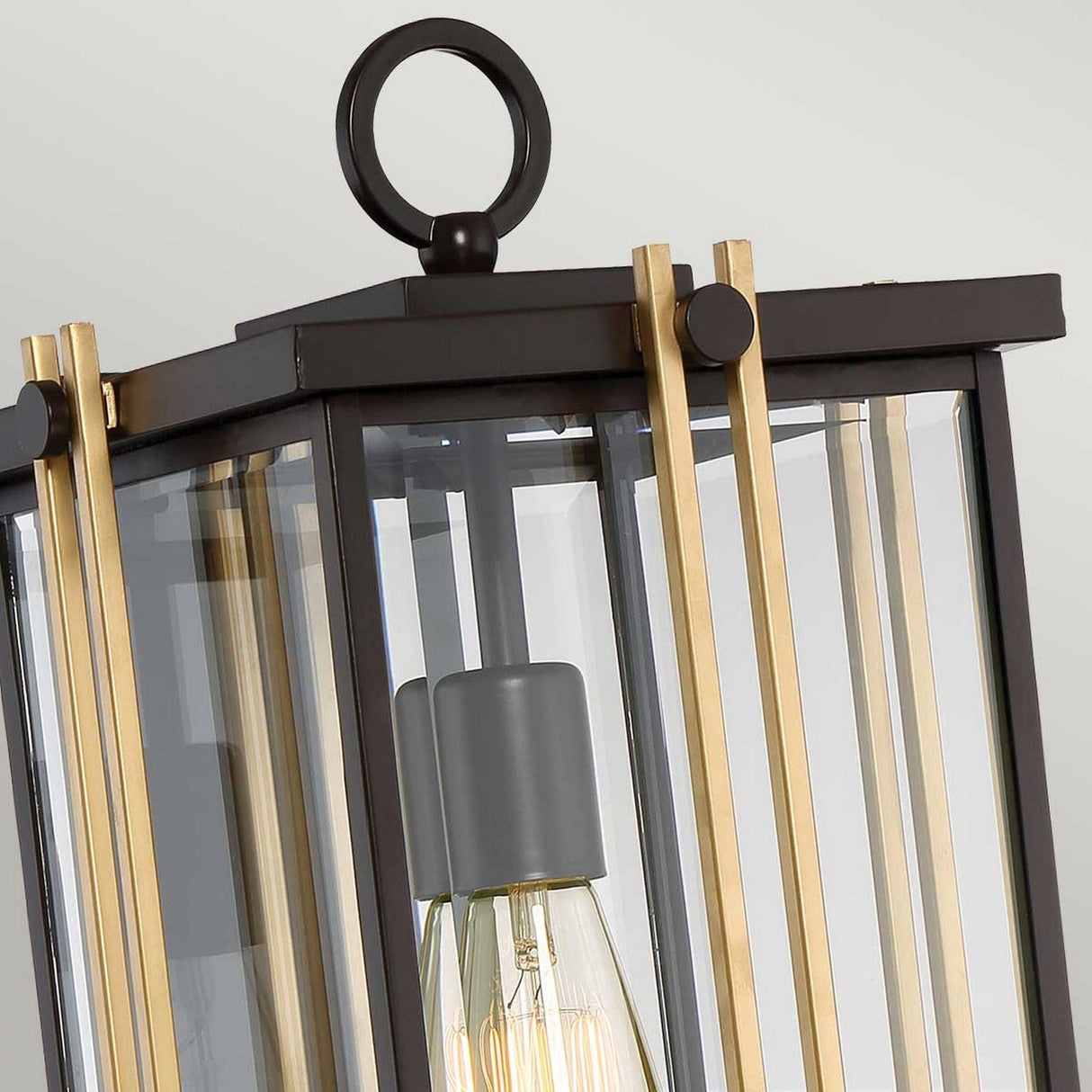 A detailed view of the Goldenrod Outdoor 1 Light Large Wall Lantern reveals its sleek Western Bronze finish, complemented by a black metal frame and clear glass panels. Inside hangs a prominent Edison bulb. The fixture is topped with a circular metal handle, echoing the robust design typical of outdoor wall lanterns with an IP44 rating for enhanced durability.