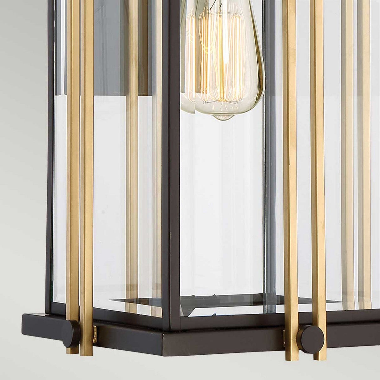 Close-up of the Goldenrod Outdoor 1 Light Large Wall Lantern, showcasing a clear glass casing, vertical gold bars, and an exposed filament bulb, elegantly enclosed in a rectangular black metal frame with a touch of Western Bronze finish.