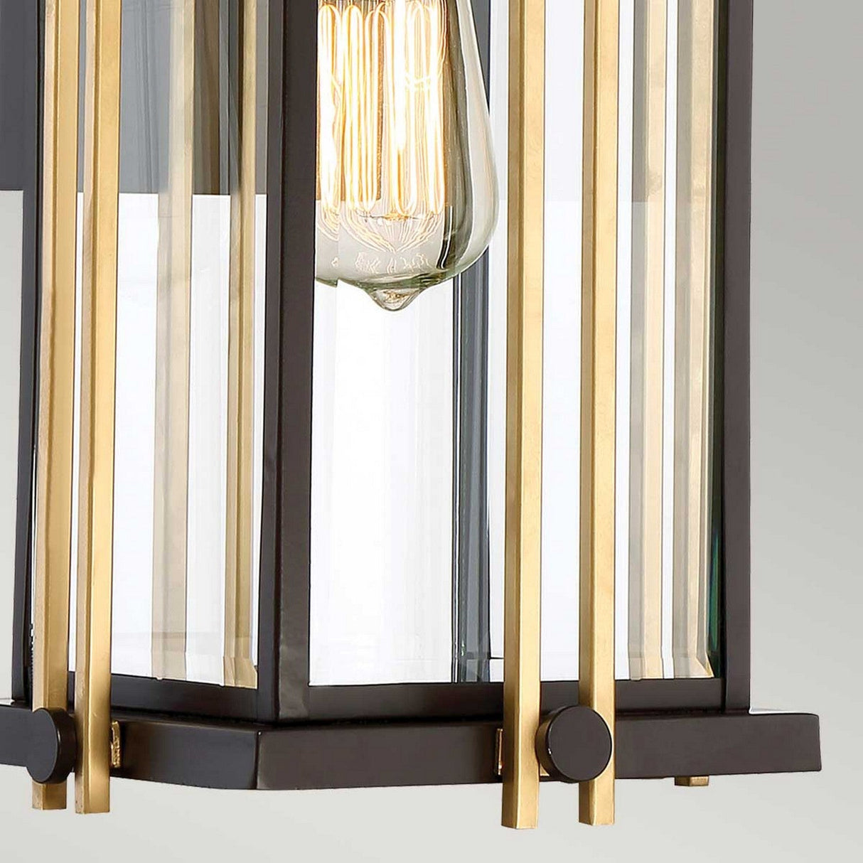Close-up of a Goldenrod Outdoor 1 Light Medium Wall Lantern in bronze, showcasing a clear, geometric, glass-encased bulb. The lantern's black and gold accents exude modern style reminiscent of Mid-Century lighting, blending elegance with contemporary flair.