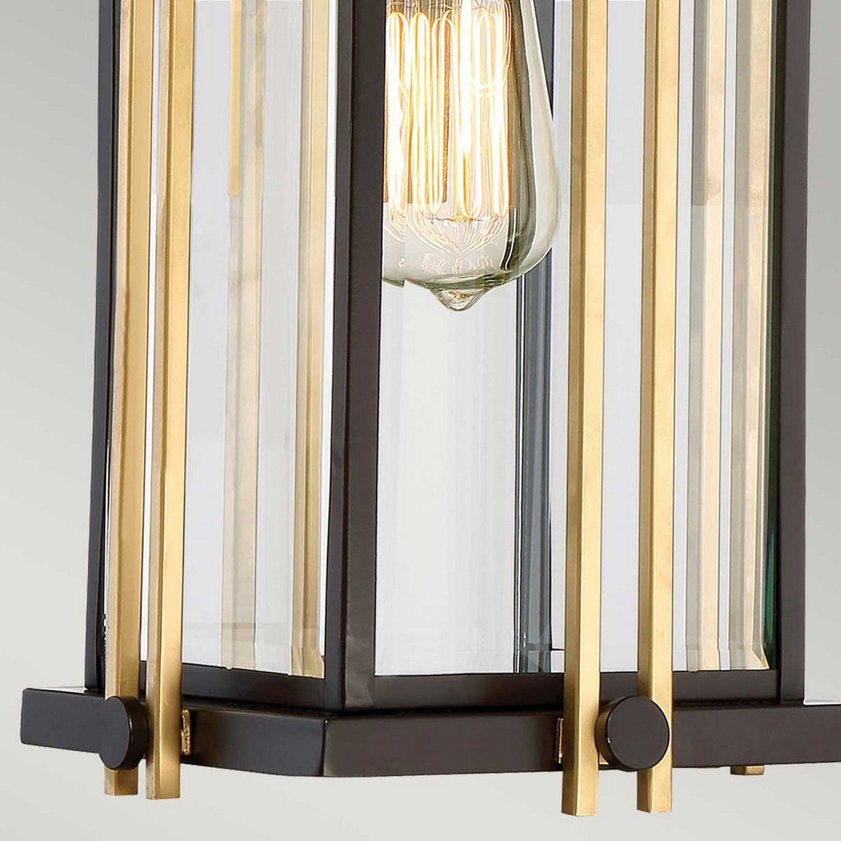 A close-up of the Goldenrod Outdoor 1 Light Medium Chain Pendant highlights its decorative light fixture with a vintage-style exposed bulb encased in a frame accented with Western Bronze and clear glass panels. The pendant's modern geometric design is reminiscent of mid-century lighting, showcasing the intricate filament of the bulb.