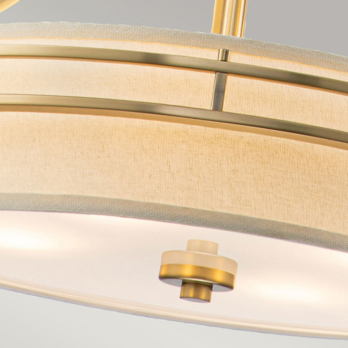 Close-up of the Gotham 4 Light Small Chandelier - Brushed Brass with a cream shade. The design showcases horizontal brushed brass rods and a circular shape, offering a stylish and contemporary aesthetic. The light emits a soft glow.