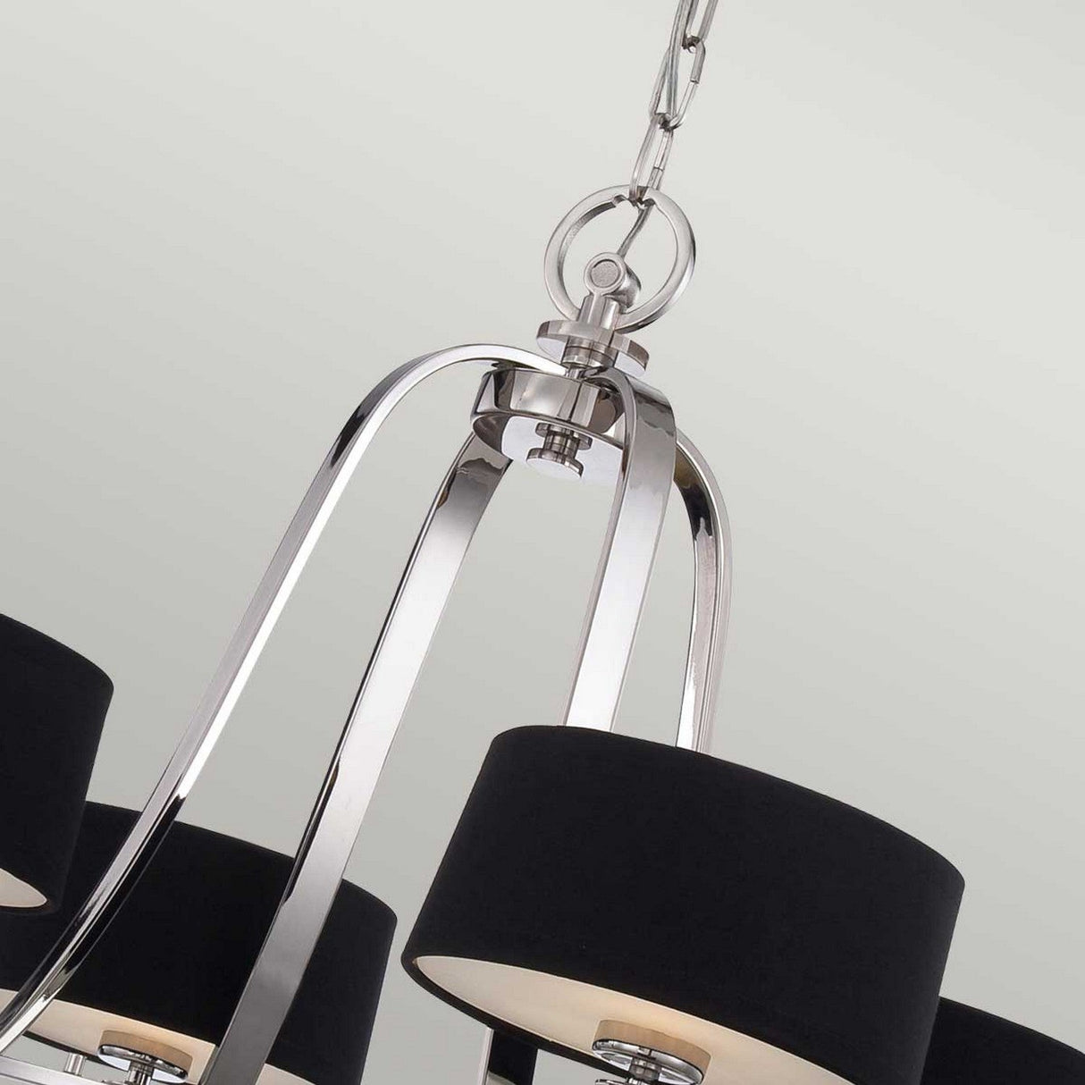 A close-up of the Gotham 4 Light Chandelier - Imperial Silver highlights its industrial elegance with a silver metallic frame and four black cylindrical lampshades. Suspended by a linked chain, this masterpiece in Imperial Silver stands out against a plain light background.