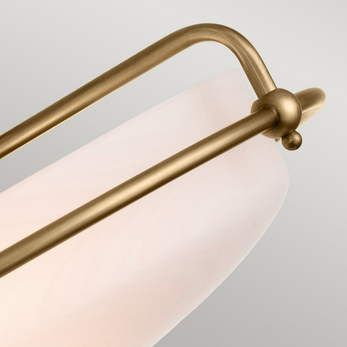 A close-up of the Griffin 3 Light Flush in weathered brass, showcasing its opaque etched glass shade. This elegant design highlights curved lines and spherical accents, making it ideal for transitional interiors, all set against a light gray background.