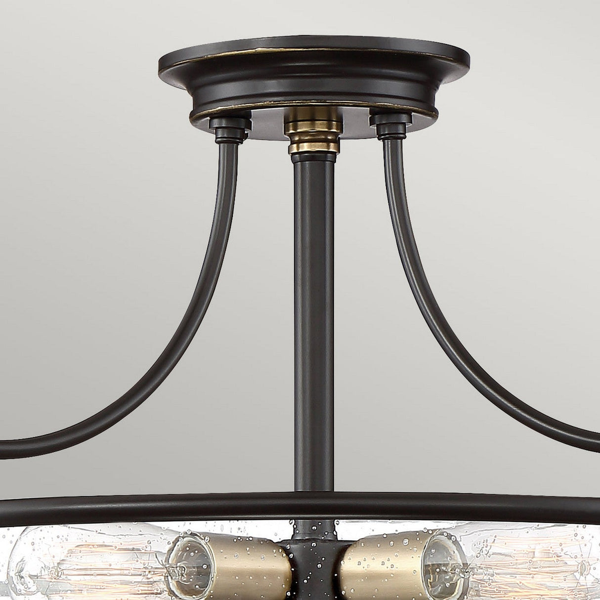 Close-up of the Griffin 3 Light Large Semi-Flush in Palladian Bronze with Weathered Brass accent, showcasing three Edison-style bulbs nestled within clear, seeded glass shades. The fixture features a metallic base with elegantly curved support arms, lending a modern industrial aesthetic against a neutral backdrop.
