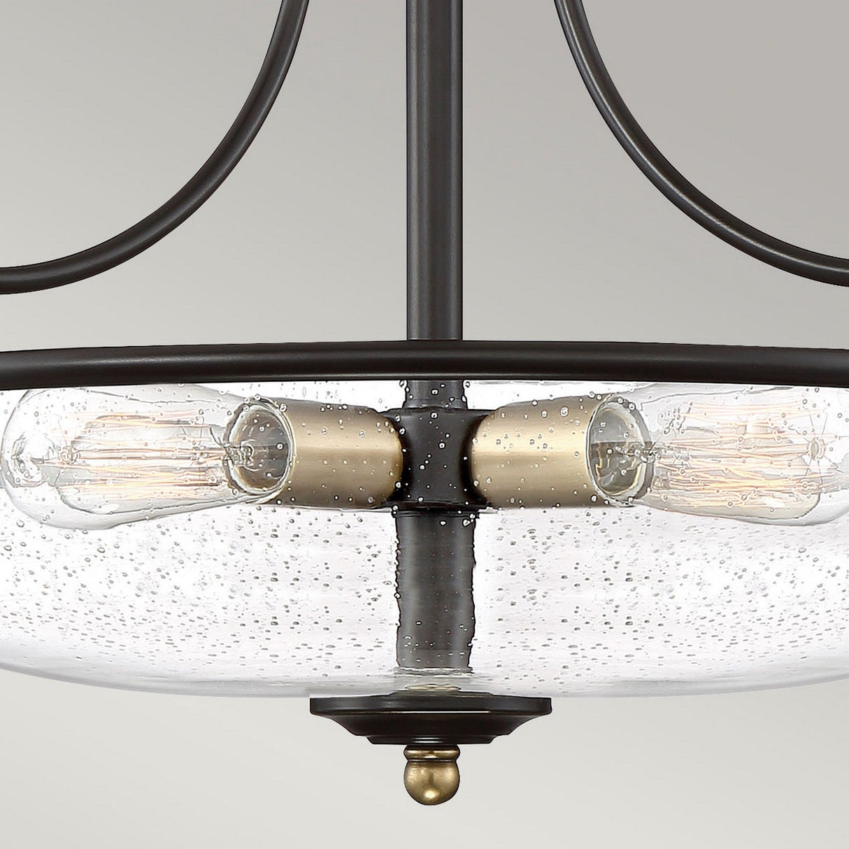 A close-up of the Griffin 3 Light Large Semi-Flush, featuring a clear, textured glass bowl with Edison-style filament bulbs inside. The frame boasts a Palladian Bronze finish with weathered brass accents, set against a plain light gray background.